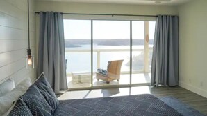 Une chambre avec un grand lit, une vue sur la mer par une porte-fenêtre coulissante et un fauteuil sur le balcon.