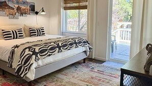Un dormitorio con una cama, un ventilador de techo, una ventana con cortinas, una alfombra y un cuadro en la pared.