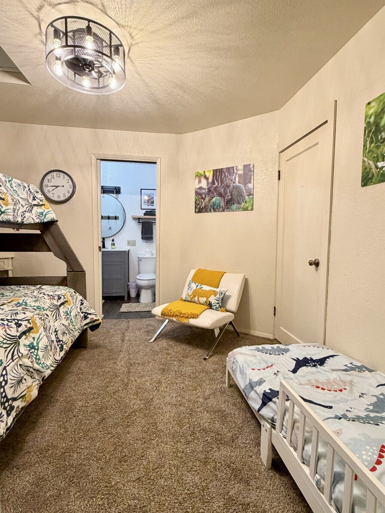 Une chambre avec des lits superposés, une chaise avec un coussin, une porte et une horloge murale.