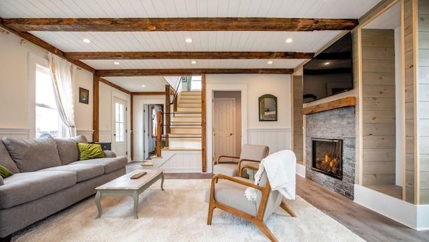 Una sala de estar con chimenea, vigas de madera, un sofá y una escalera.