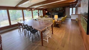 Een ruime eethoek met een grote houten tafel en stoelen, een open haard en grote ramen met uitzicht op de omgeving.