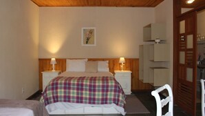 A bedroom with a wooden ceiling, a bed with a plaid blanket, two bedside tables with lamps, a nightstand, and a door leading to another room. - Casinha no sítio Calmamente  (Teresópolis)