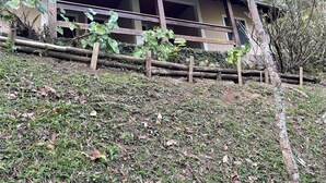 A building with a wooden porch, surrounded by greenery and a fence. - Casinha no sítio Calmamente  (Teresópolis)