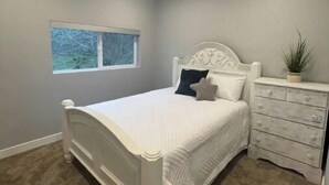 A bedroom with a white bed, a nightstand, and a window. - Peaceful Escapes and Retreats (Battle Ground)