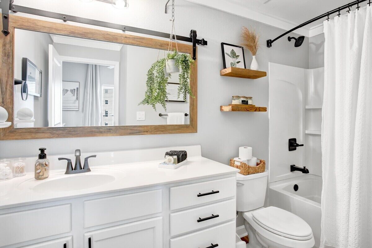 Une salle de bain moderne avec un meuble-lavabo blanc, un grand miroir, une plante suspendue et une baignoire dotée d’un rideau de douche.