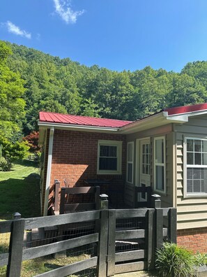 A brick house with a red roof, a wooden fence, and a view of a forested hillside. - Creekfront Cabin • Fire Pit • Fenced Yard • Near Crabtree Falls (Tyro)