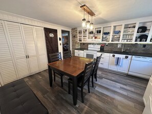 Une cuisine avec des meubles blancs, une table à manger en bois et un banc noir.