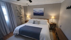 A bedroom with a large bed, two bedside tables with lamps, a wooden bench, a plant, and a painting on the wall. - Creekfront Cabin • Fire Pit • Fenced Yard • Near Crabtree Falls (Tyro)
