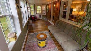 A cozy living room with a couch, a red chair, and a large window. - Creekfront Cabin • Fire Pit • Fenced Yard • Near Crabtree Falls (Tyro)