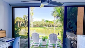 Ein Zimmer mit Schreibtisch, Computer und zwei Stühlen, mit Blick auf eine Glastür zu einem Garten mit Teich und Palmen.