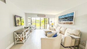 A spacious living area with a sofa, a coffee table, and a TV mounted on the wall. There is a sign that reads "THIS IS OUR HAPPY PLACE" and a large abstract painting above the sofa.