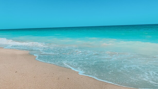 Ein Strand mit klarem türkisblauem Wasser und sandigem Ufer.