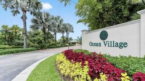 Schild für Ocean Village mit einer angelegten Grünfläche mit roten und gelben Pflanzen.