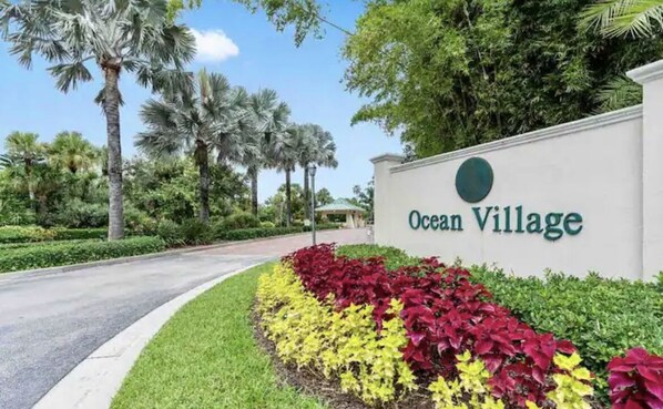 A sign for Ocean Village with a landscaped area featuring red and yellow plants.