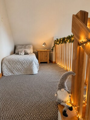 Een slaapkamer met een bed, nachtkastje, lamp, pluchen speeltje en een decoratieve slinger.