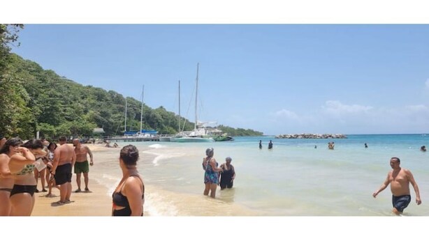 Une plage avec des gens, des bateaux et un ciel dégagé.