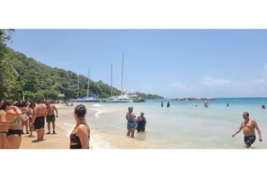 Una playa con gente, barcos y un cielo despejado.