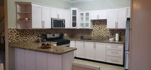 Una cocina con armarios blancos, microondas, estufa y encimera de granito.