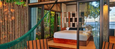 A bedroom with a large bed, a hammock, and a view of the outdoors.