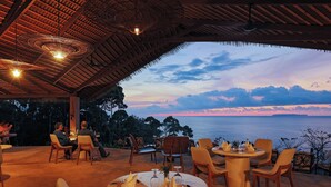 An outdoor dining area with tables set for two, overlooking a scenic view of the sea at sunset. - Corcovado Wilderness Lodge by SCP (Drake Bay)