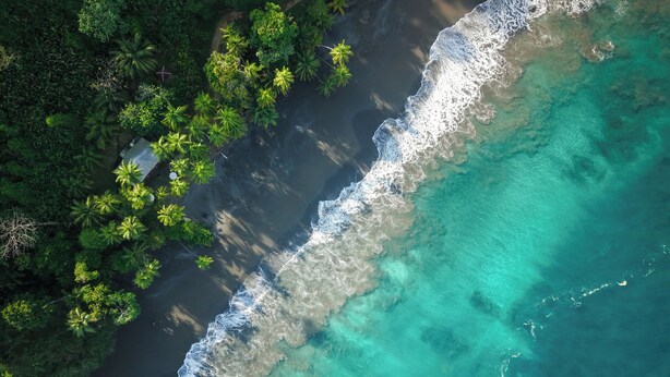 An aerial view of a coastal area with clear turquoise waters, dense green vegetation, and a rocky shoreline. - Corcovado Wilderness Lodge by SCP (Drake Bay)
