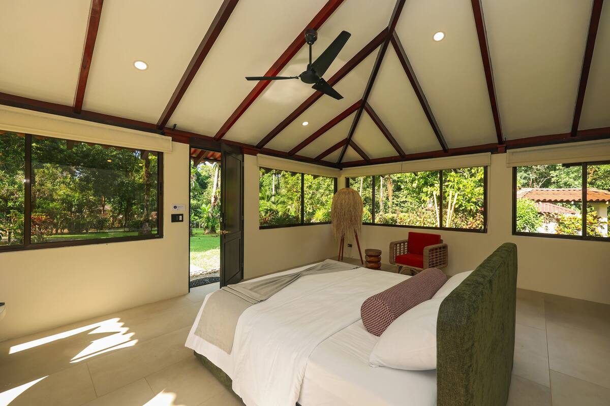 Een ruime slaapkamer met een groot bed, een plafondventilator en grote ramen met uitzicht op het landschap.