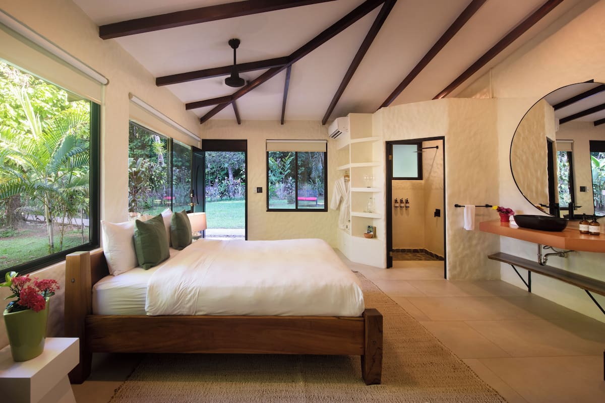 Een moderne slaapkamer met een groot bed, een badkamer met douche, en uitzicht op een tuin.