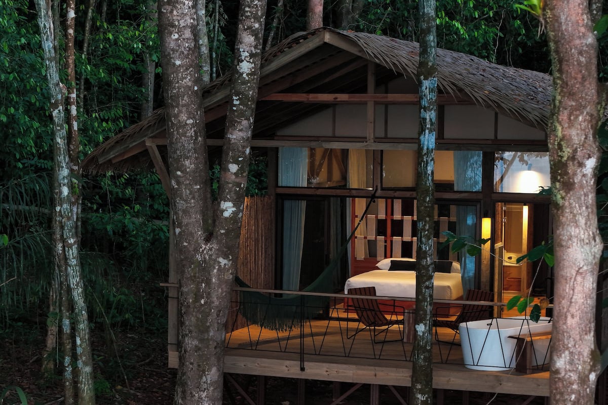 Een houten hut met een balkon, een bed en een zithoek.