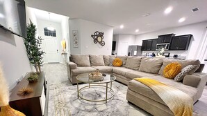 Una sala de estar moderna con un sofá seccional, una mesa redonda de centro y un comedor con una mesa y sillas.