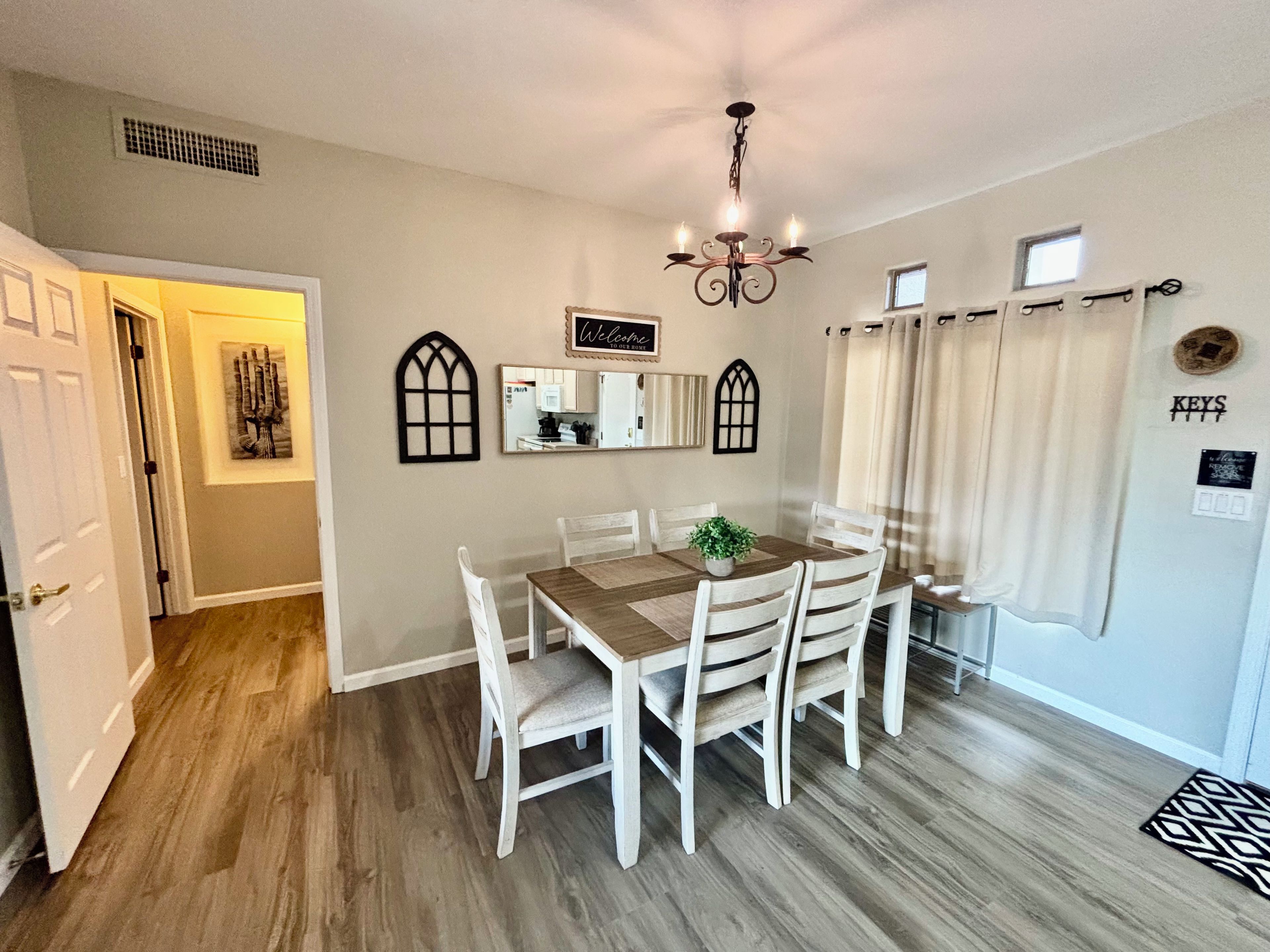 A dining area with a wooden table, white chairs, a chandelier, and a mirror on the wall.