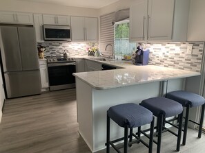A modern kitchen with stainless steel appliances, a large island with bar stools, and a tiled backsplash. - Remote Worker? Retired? Storm Tracker? +Own Canal Dock (Ocean Shores)