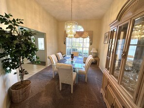 Uma sala de jantar com mesa de vidro, cadeiras estofadas, um candelabro e um armário com portas de vidro.
