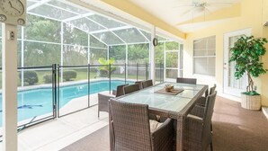 Eine überdachte Terrasse mit einem Glastisch und Korbstühlen, mit Blick auf einen Swimmingpool.