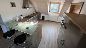 A modern kitchen with a wooden ceiling, a window with a view, and a dining area with two chairs. - Vacation apartment in a quiet location (Schwabmünchen)