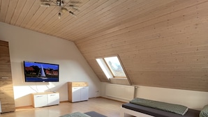 A modern loft bedroom with a sloped ceiling, a TV mounted on the wall, a bed with a green patterned bedspread, and a small seating area with a bench. - Vacation apartment in a quiet location (Schwabmünchen)