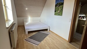 A small, sloped ceiling room with a bed, a radiator, a rug, and a picture on the wall. - Vacation apartment in a quiet location (Schwabmünchen)