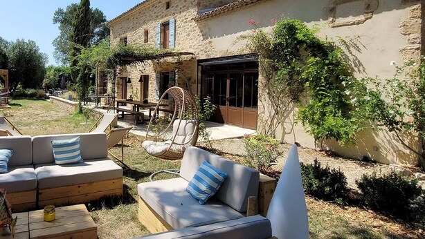 Un bâtiment rustique en pierre doté d’un espace extérieur aménagé, comprenant un canapé et des fauteuils, ainsi qu’une chaise suspendue.