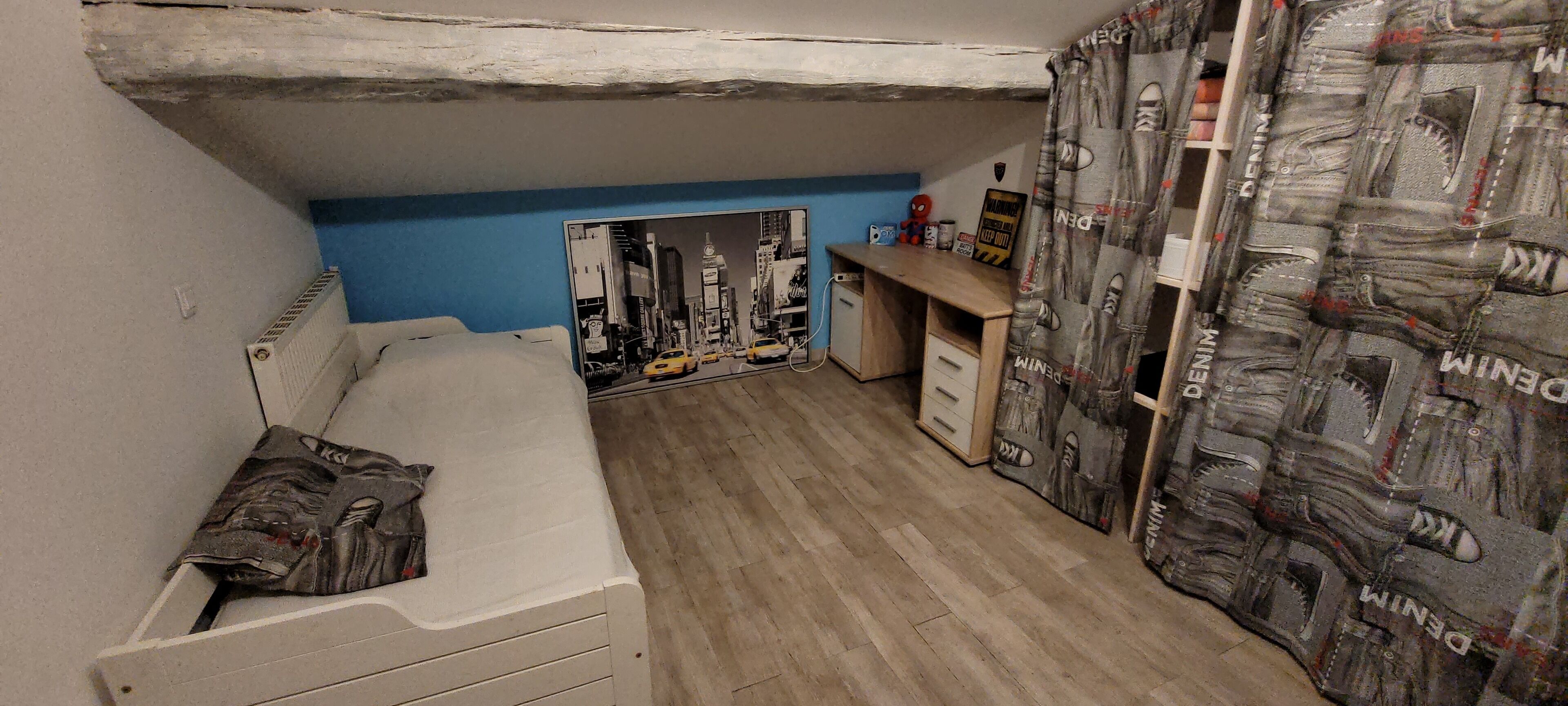 A small bedroom with a single bed, a desk, and a chair. There is a poster on the wall and a curtain with a denim pattern.