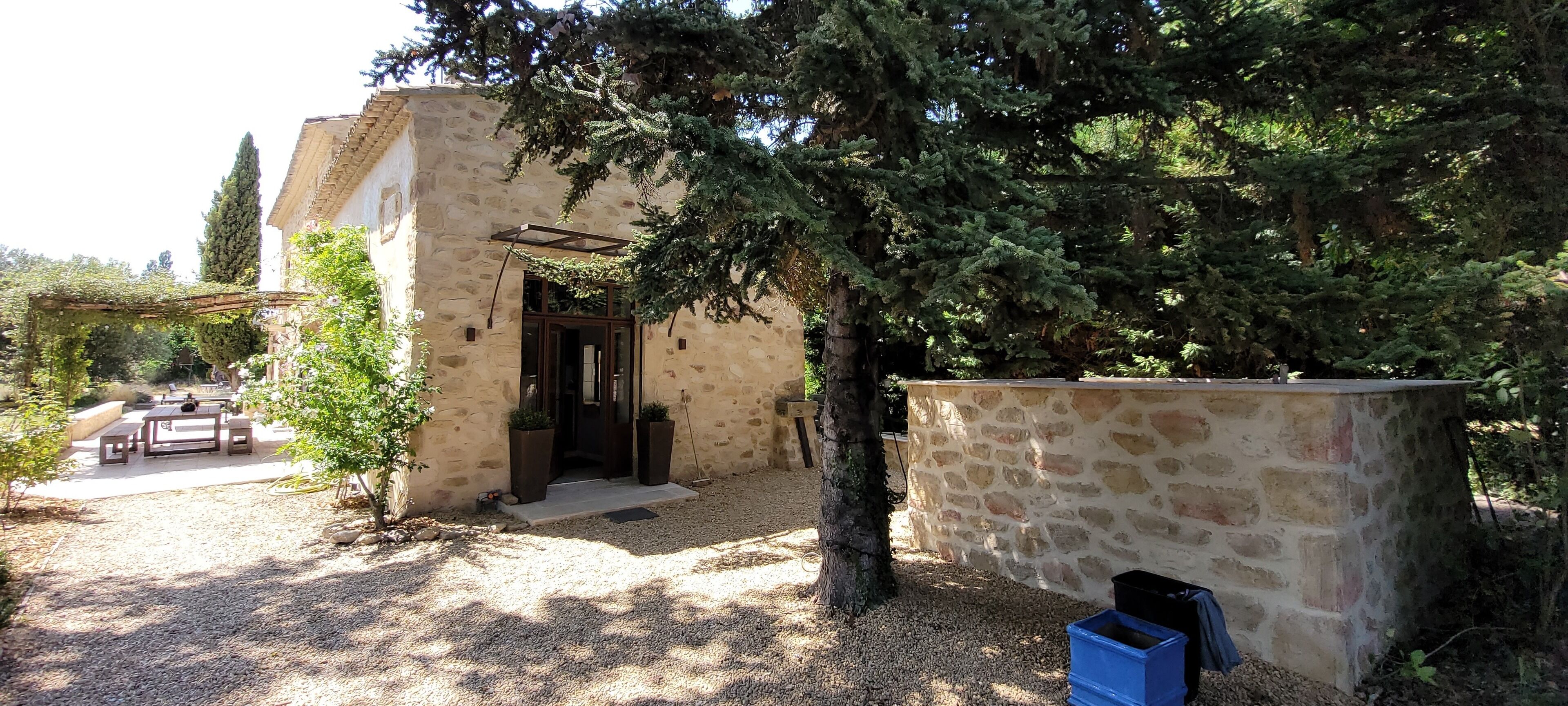 A stone building with a wooden door, a covered outdoor seating area, and a gravel path.
