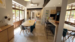 Une cuisine spacieuse dotée d’un îlot central, de grandes fenêtres et d’un coin repas avec des chaises et une table.