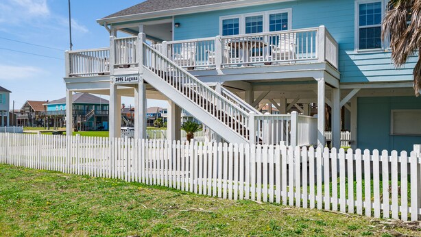 A two-story house with a white picket fence, a balcony, and a staircase leading to the second floor. - Great Back to School Dealsl!  4 minute walk to beach! (Bolivar Peninsula)