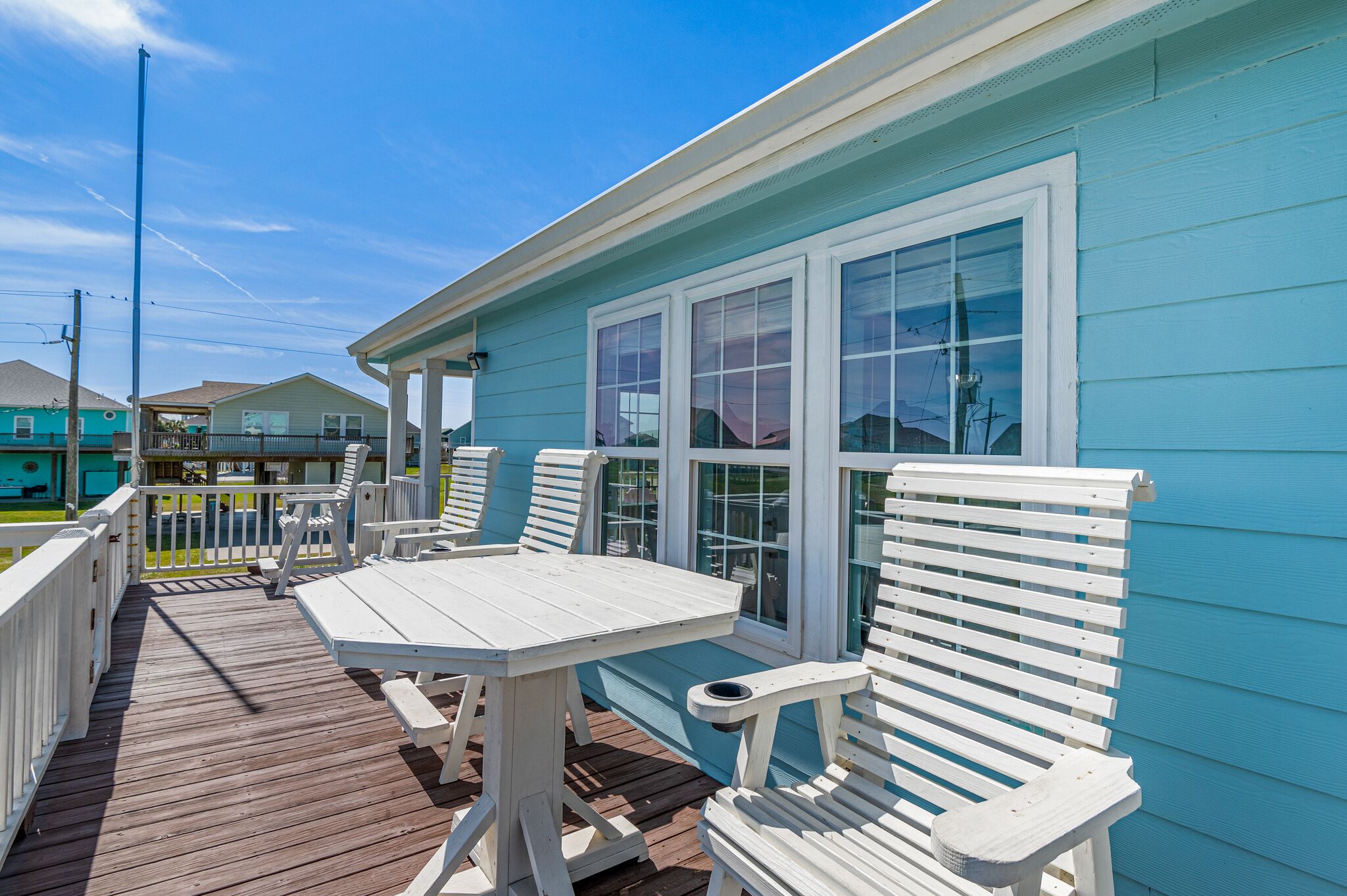 A covered deck with white furniture and a blue building.