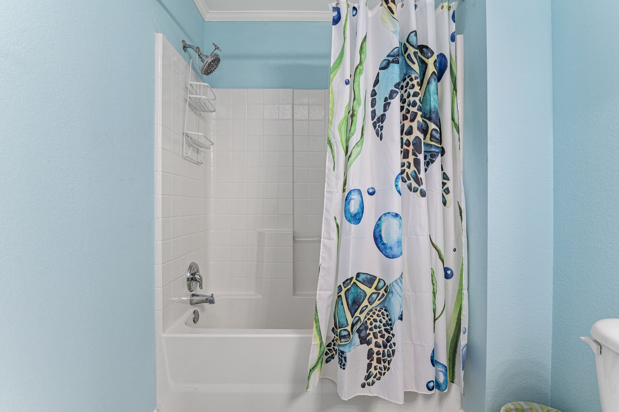 Un bagno con vasca, doccia e tenda decorata con il motivo di una tartaruga marina.