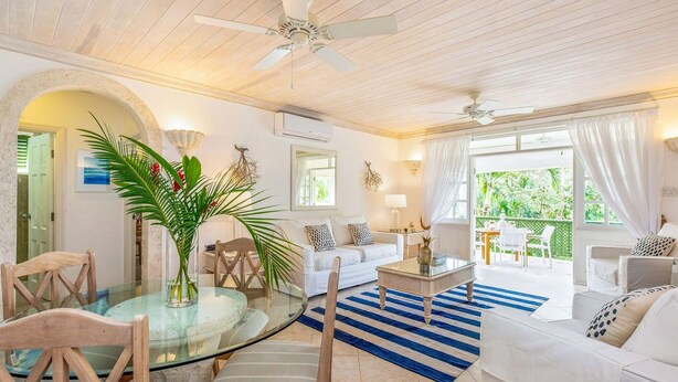 Un salón amplio con una mesa de comedor de vidrio, sofás blancos y un tapete azul a rayas.