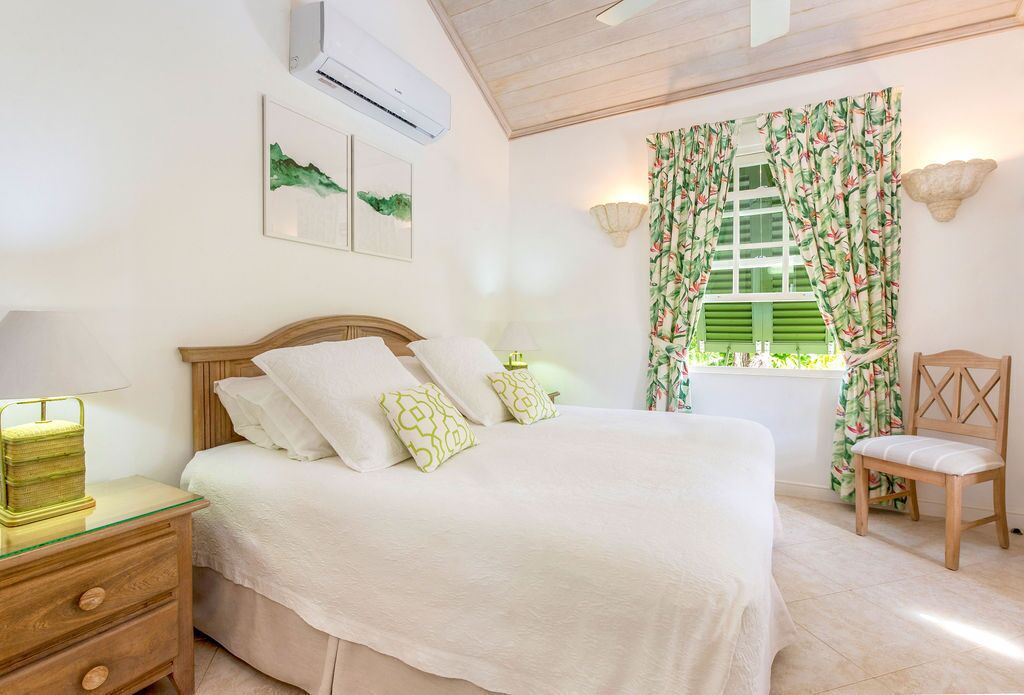 A bedroom with a bed, a nightstand, a chair, a window with curtains, and wall-mounted lights.