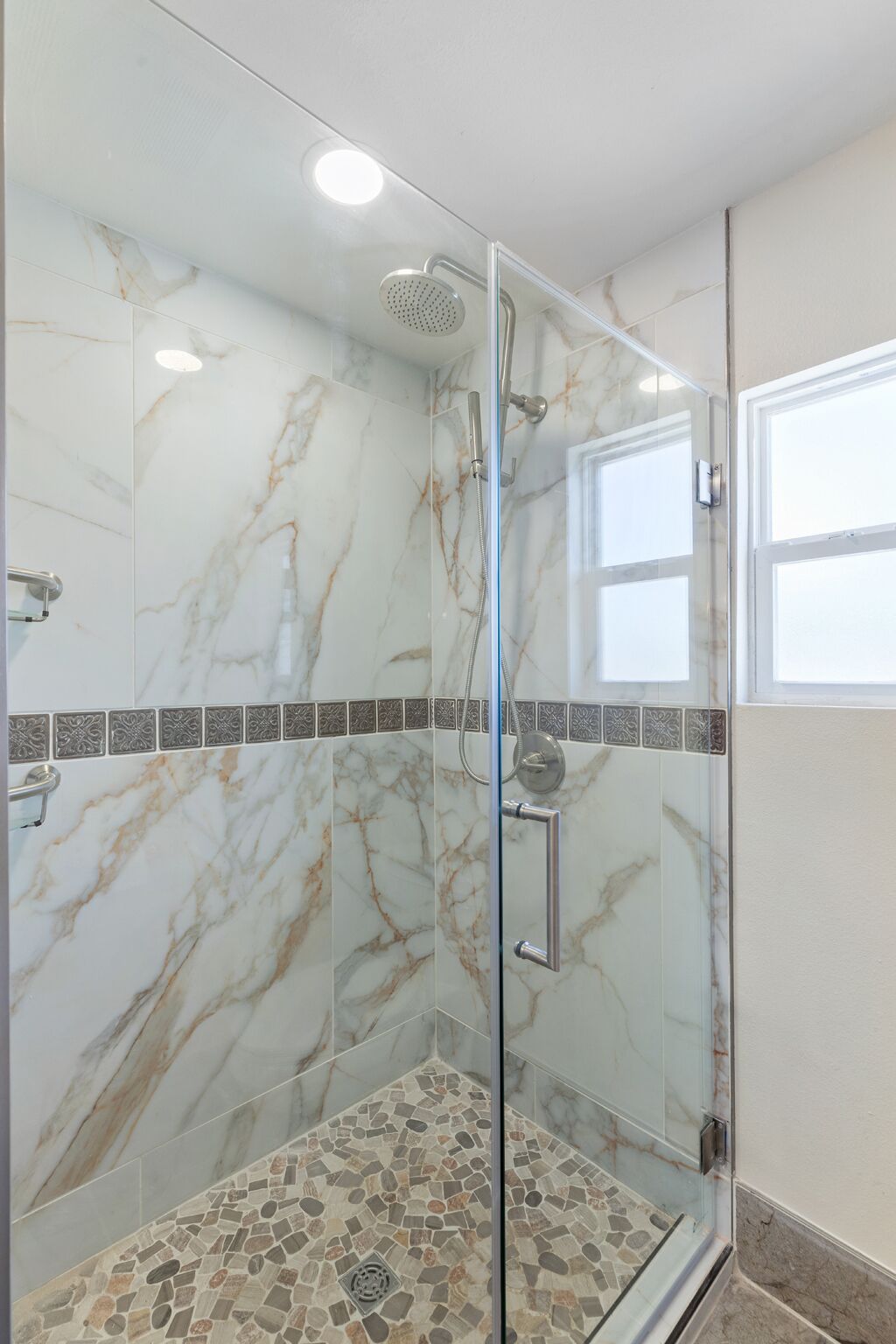 A glass-enclosed shower with a marble wall and a mosaic floor.