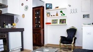 A compact kitchen with a refrigerator, stove, and a dining table with a chair. There are decorative plates and a cabinet with glass doors. - Gioia's House (Roma)