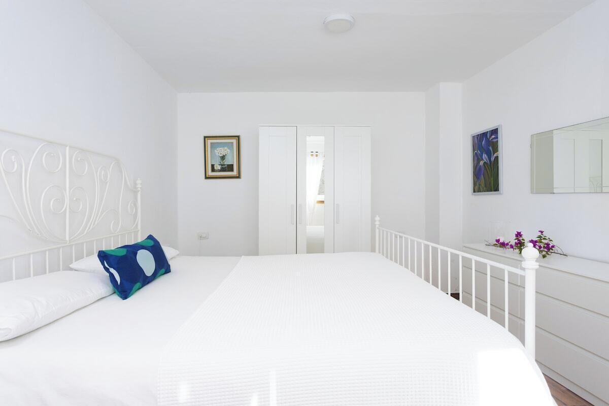 A bedroom with a white bed, white walls, a white ceiling, a white railing, a white wardrobe, and a white door.