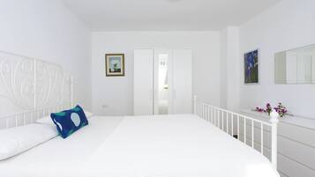 A bedroom with a white bed, white walls, a white ceiling, a white railing, a white wardrobe, and a white door.