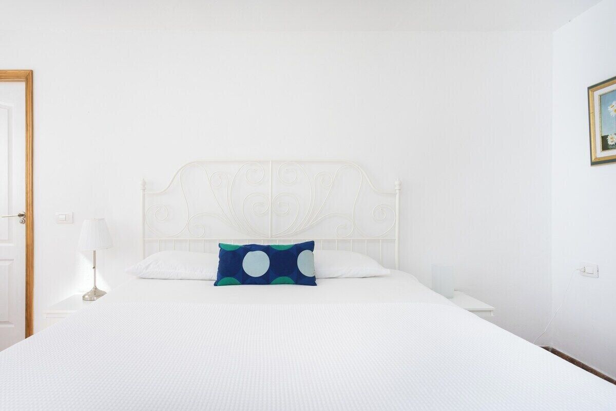 A white bed with a decorative headboard, a blue pillow with white polka dots, and a white bedside table.
